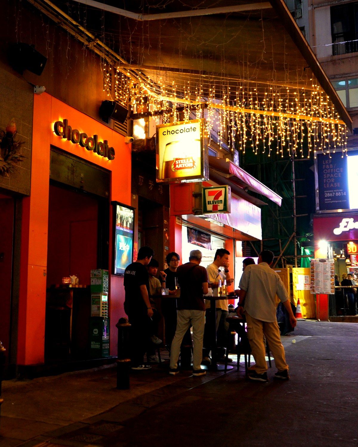 Chocolate on Lan Kwai Fong at night, the lit sign and orange frontage under the street's fairy lights