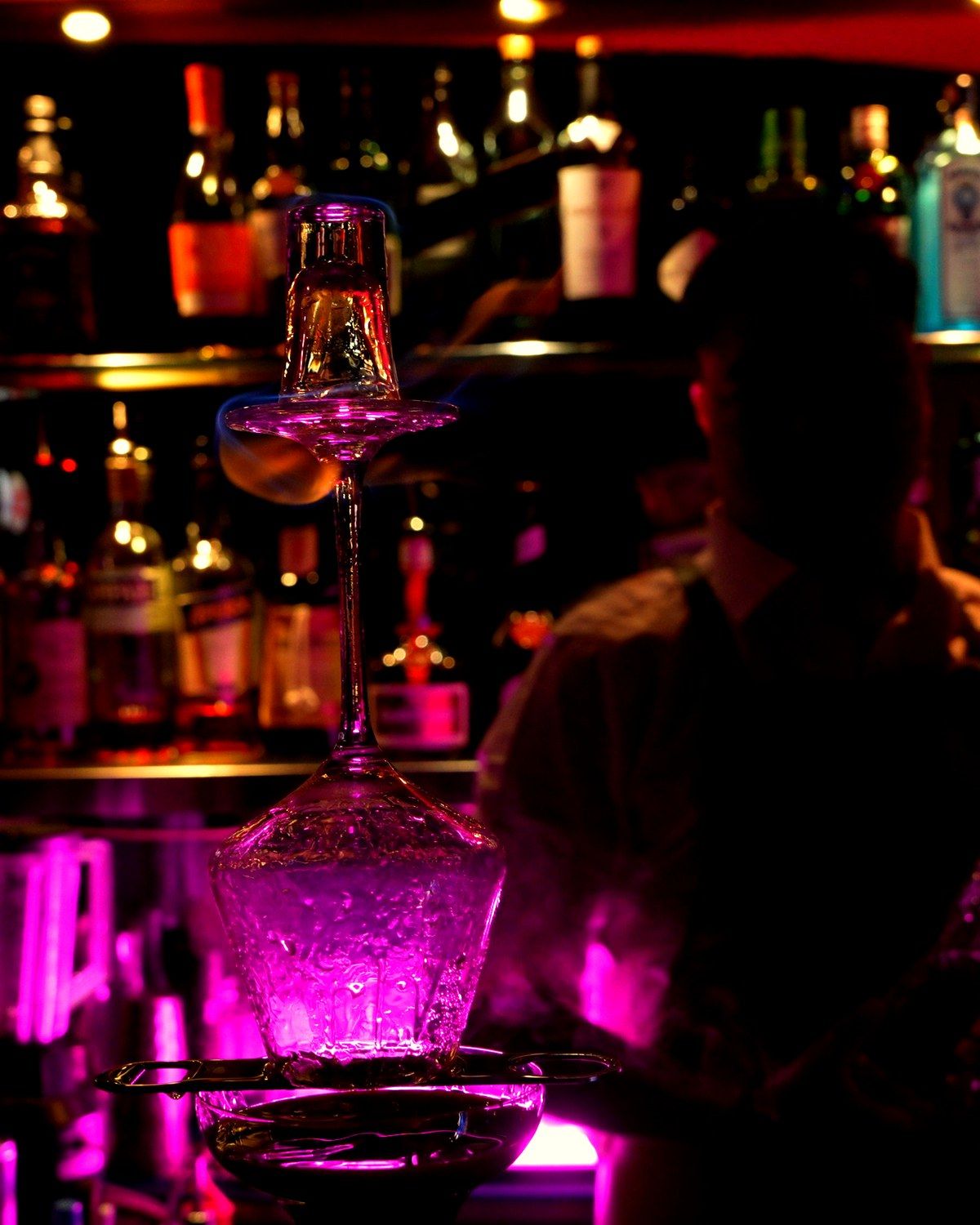 The back bar at Chocolate in low light, a glass tower glowing pink in front of the shelves
